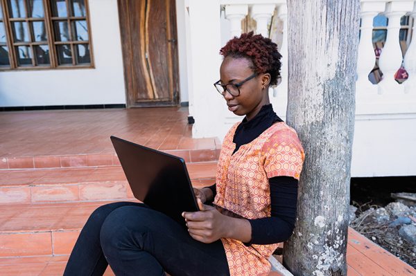 Young African female student with glasses and laptop sitting on the porch preparing for her exam