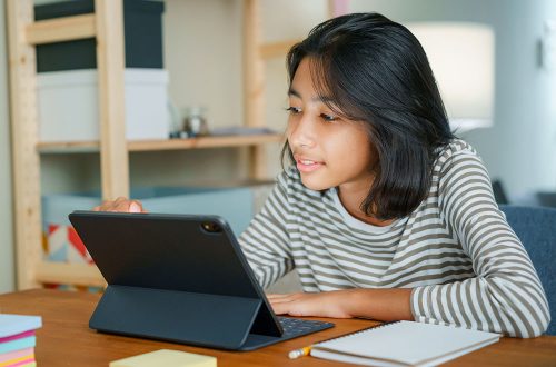 Asian girl is studying online via the internet on tablet digital while sitting at the table at night. Concept of online learning at home